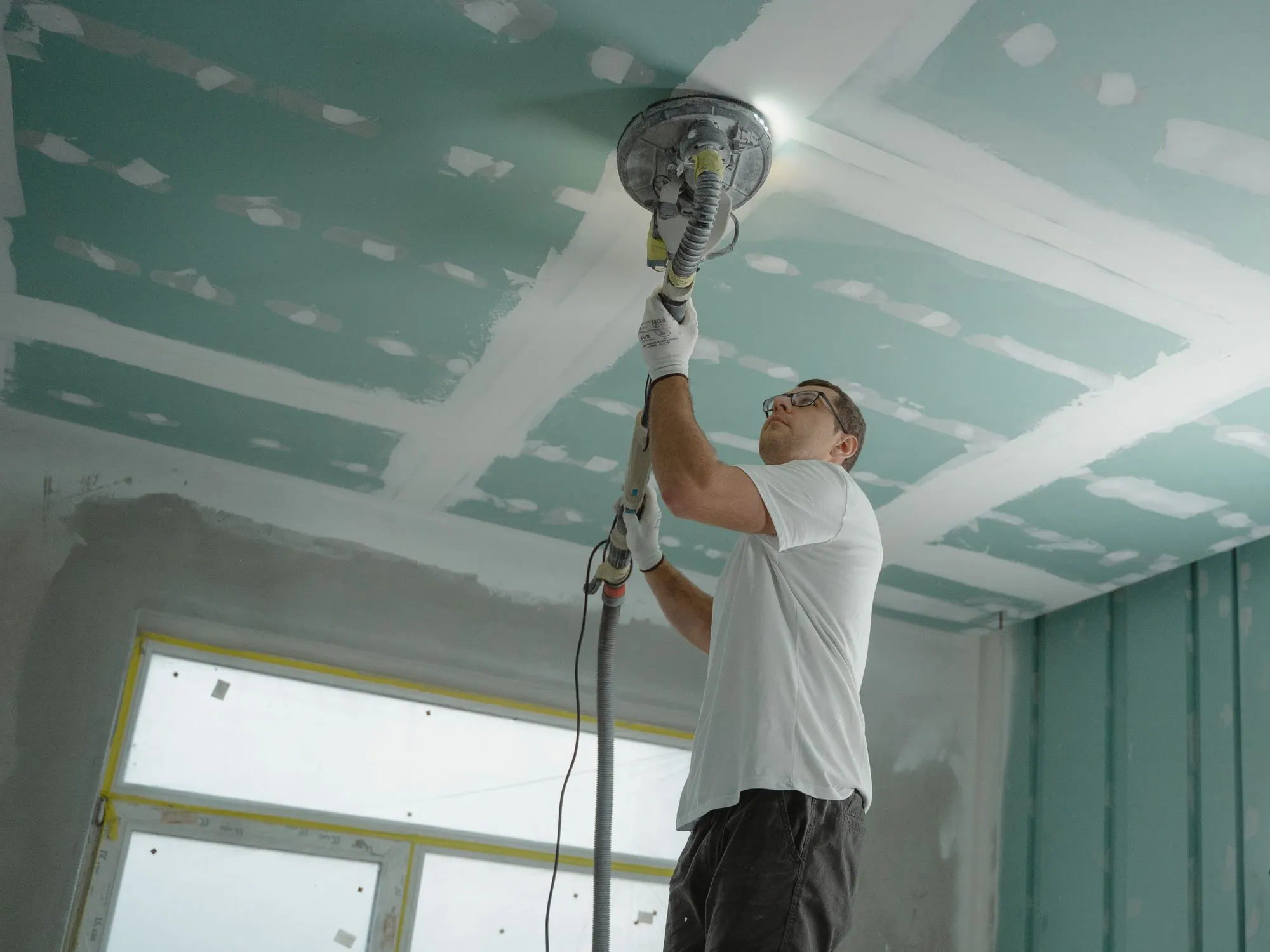 Drywall ceiling being sanded, taped and mudded joints visible